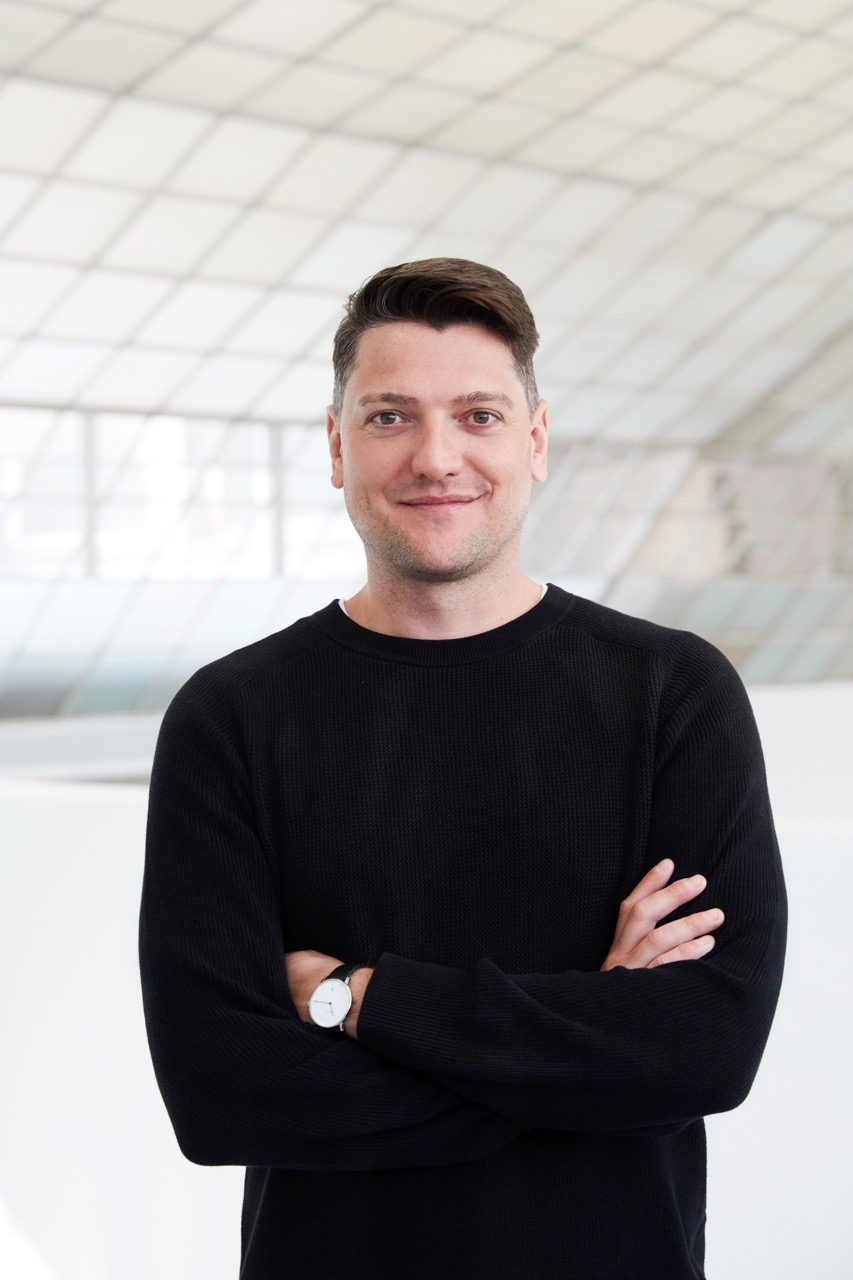 Christian Hellinger: Porträt eines Mannes mit kurzem, braunem Haar. Er trägt ein schwarzes T-Shirt und hat die Arme verschränkt. Er schaut in die Kamera und lächelt herzlich.