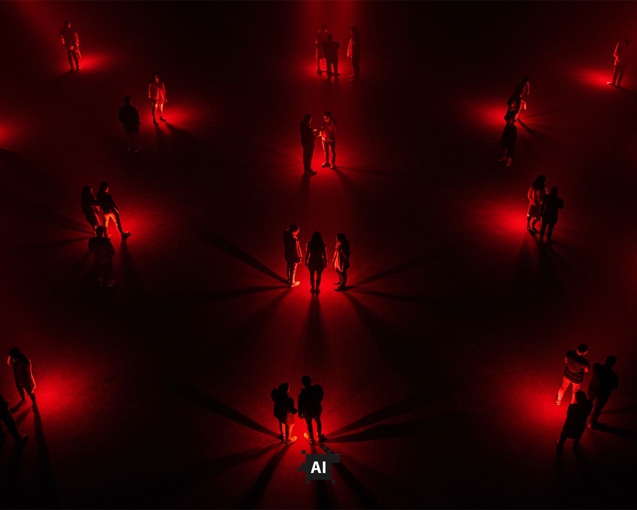 multiple small groups of people standing together in red spotlights in a dark room chatting