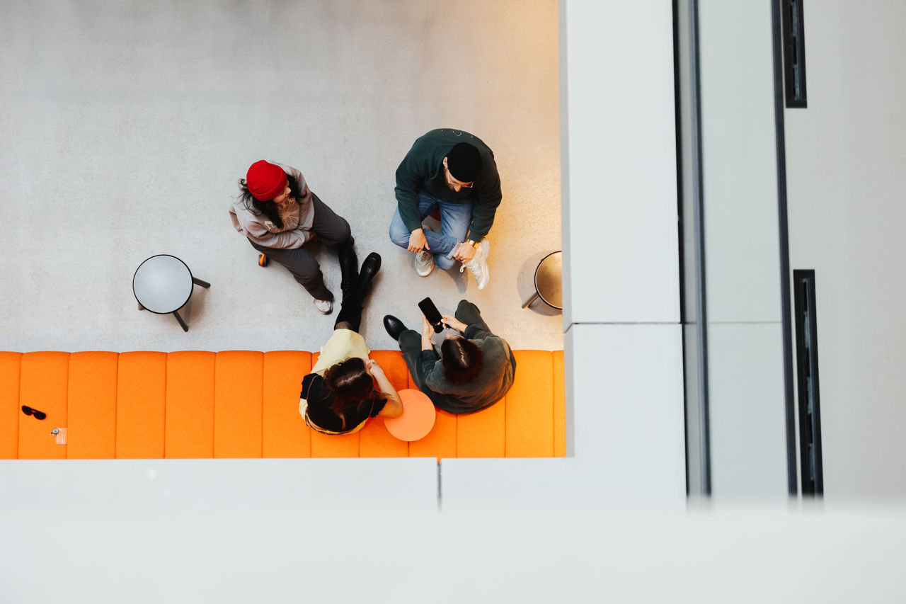Bird's eye view of a group of four people sitting on an orange couch. The scene depicts a relaxed, collaborative environment