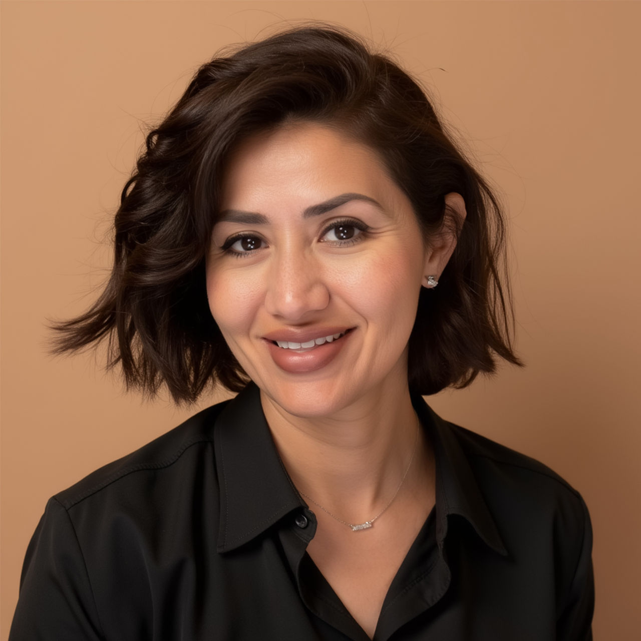 Sara Eid. Portrait of a woman with short dark hair and side parting against a beige background. She wears a black shirt and a delicate necklace.
